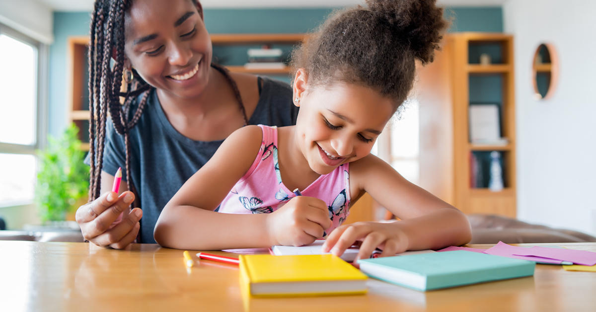 Mãe e filha estudando juntas com lápis de cor e cadernos sobre a mesa